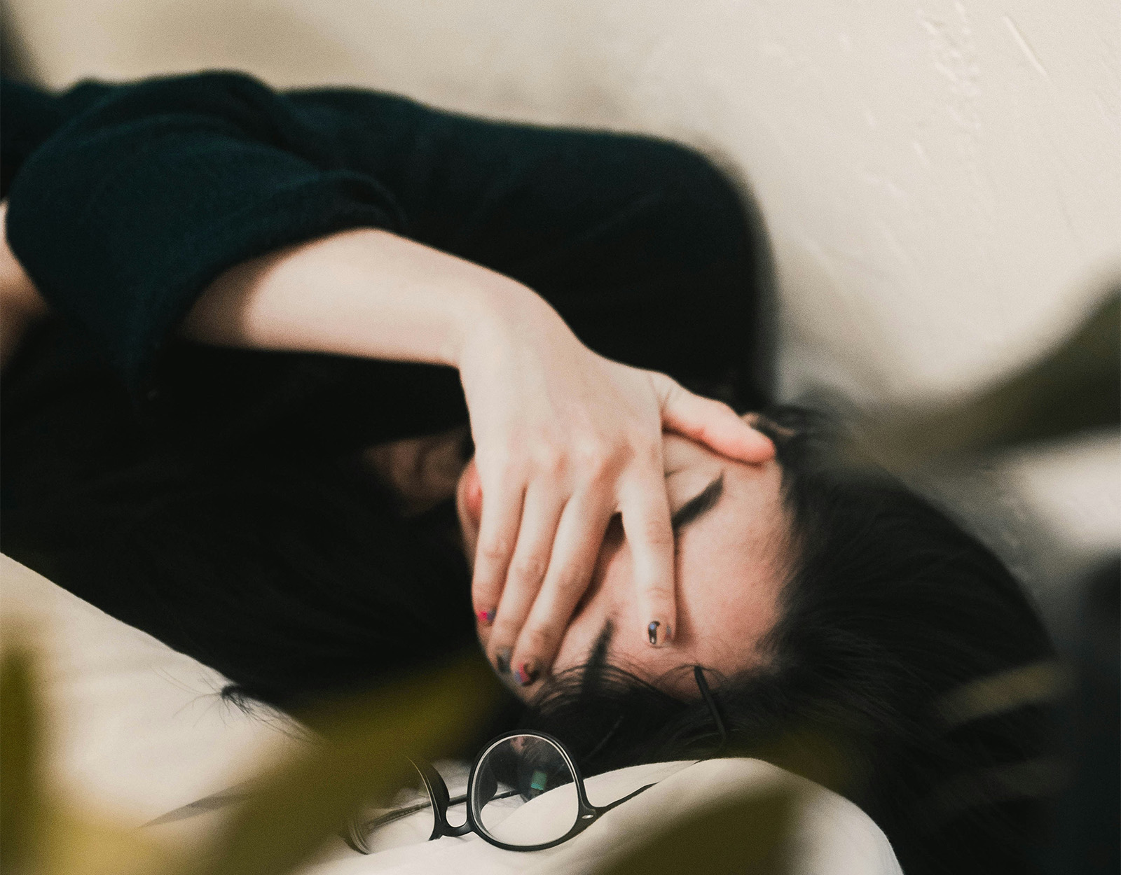a woman with her hand covering her eyes. Her glasses are laying in front of her