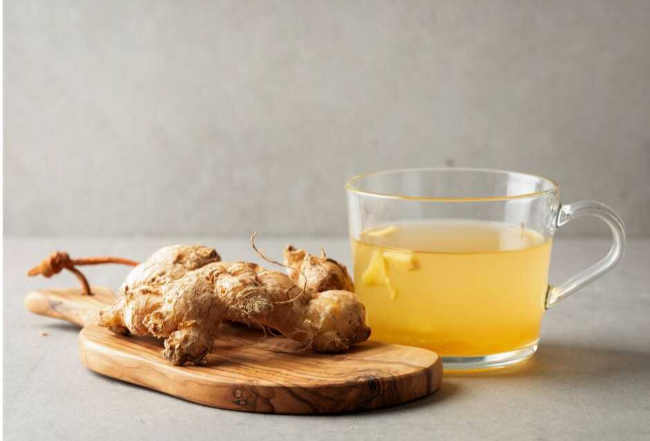 several pieces of fresh ginger beside a clear mug filled with ginger tea