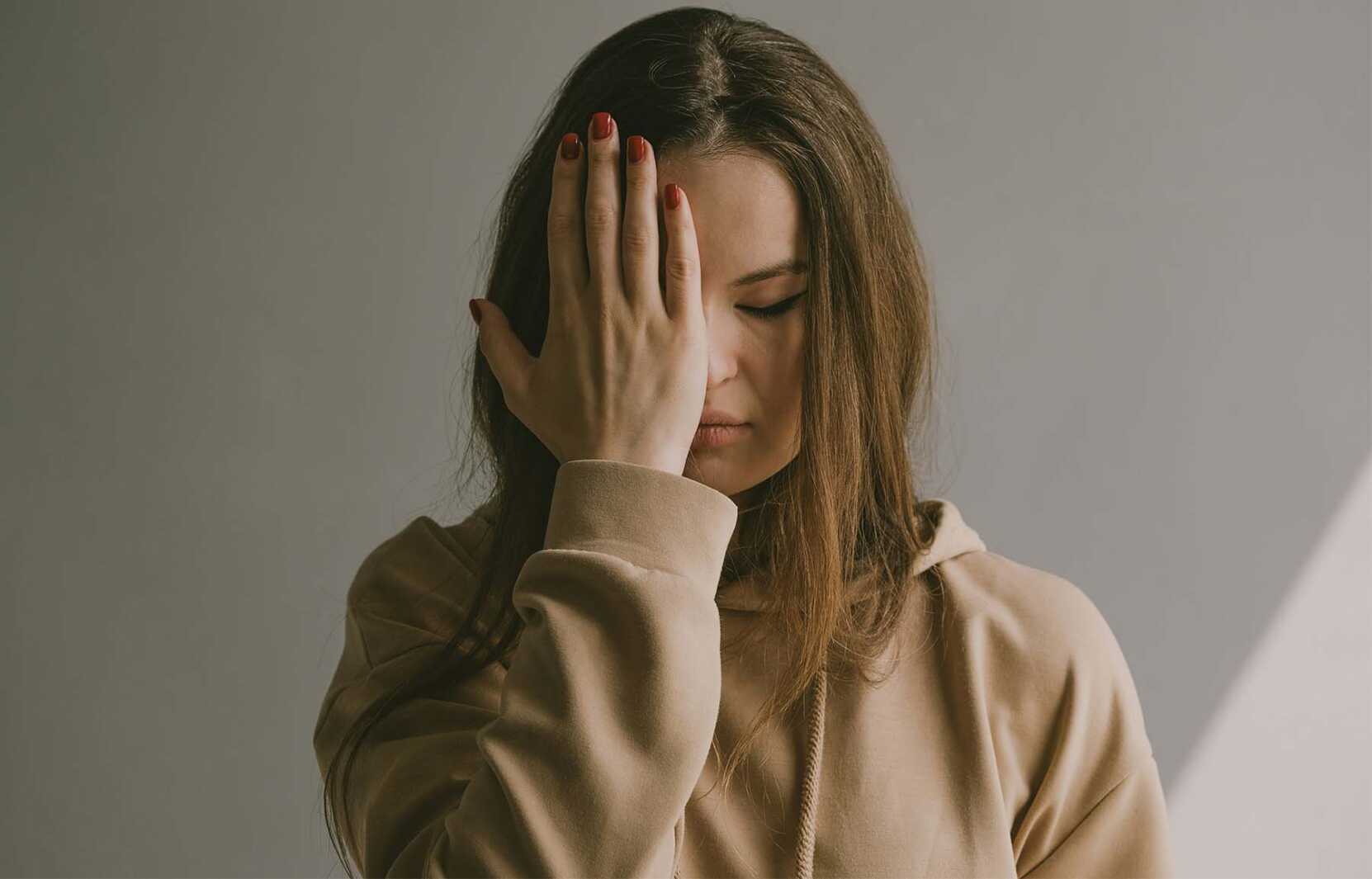 Woman with long brown hair has her eyes closed and her palm pressing against her face