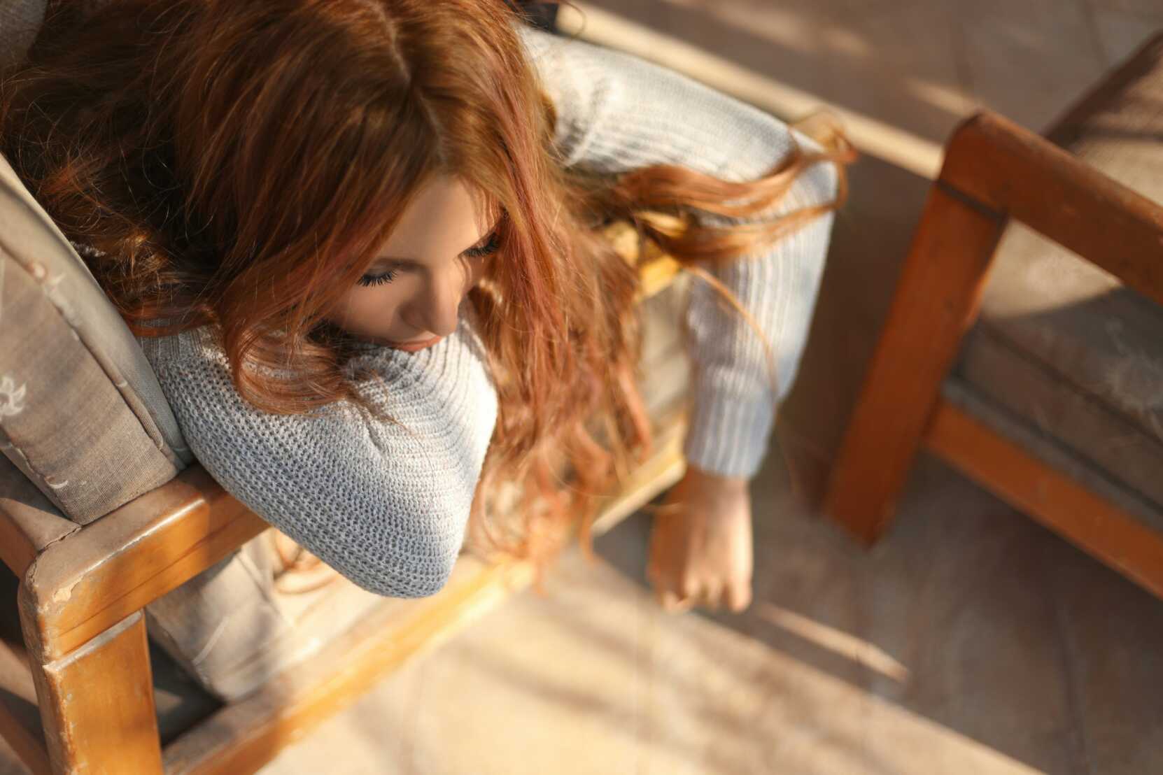 Woman with long red hair laying across a chair with a thoughtful look on her face